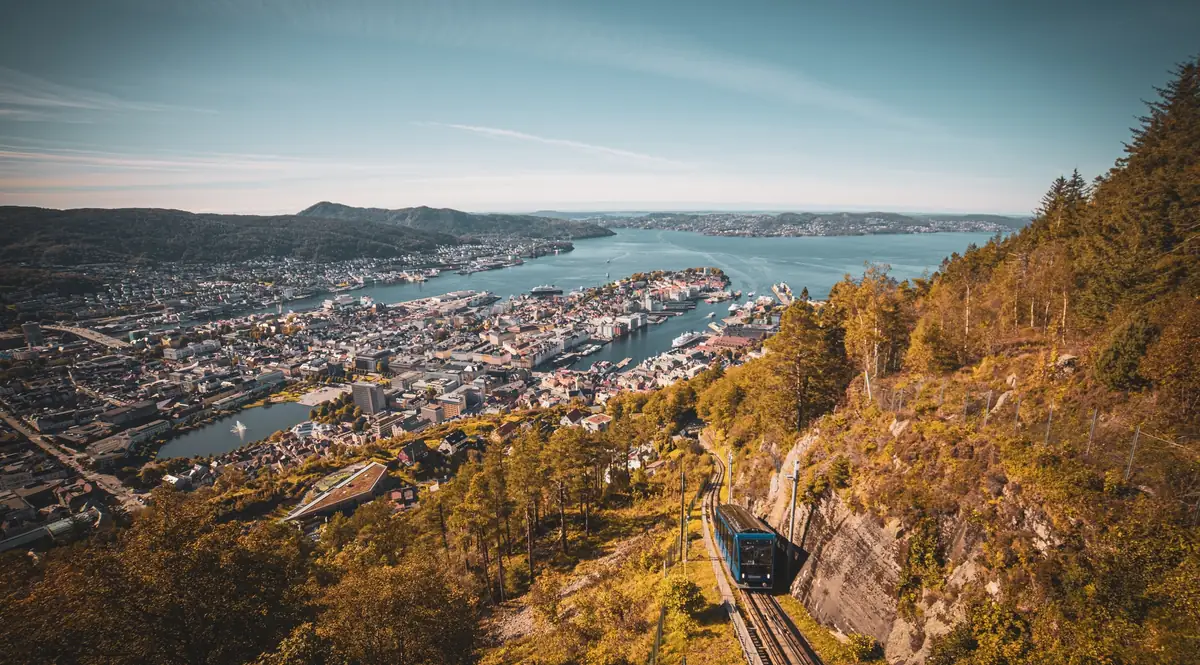 The blue Fløibanen funicular climbing above Bergen, with the harbour, the city centre and the fjord spread out below in autumn sun