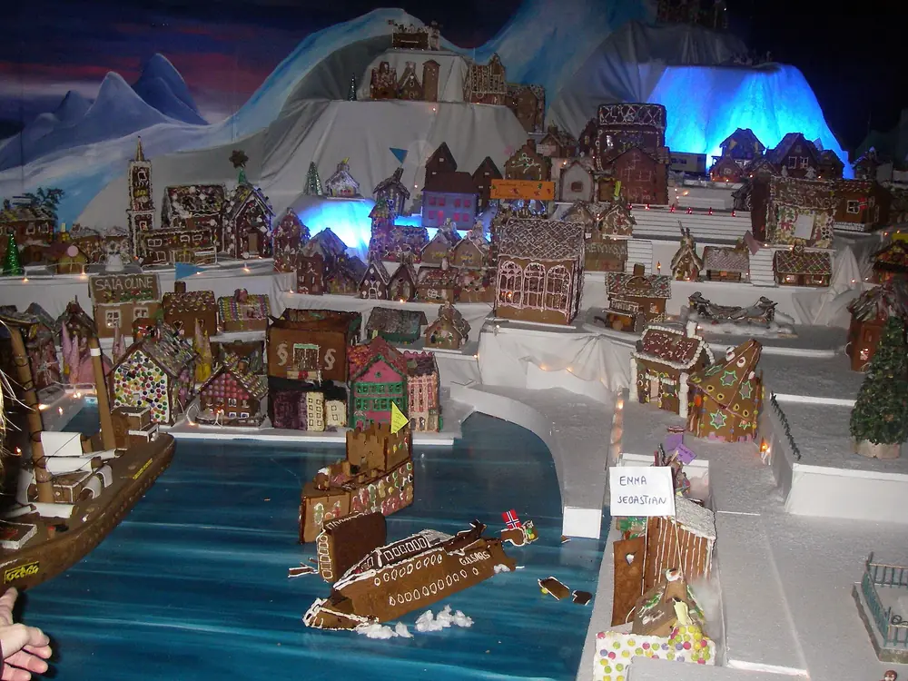 A miniature Bergen built from gingerbread, lit houses around a painted blue fjord with gingerbread ships on it