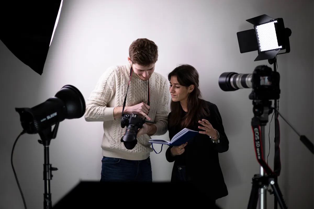 En fotograf viser bildene på kameraskjermen til en kunde i et studio med softboks og lamper